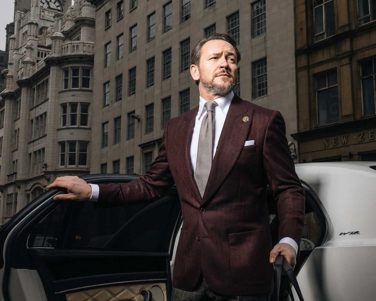 Man wearing a burgundy tailored jacket and tie beside a car on a Liverpool city street